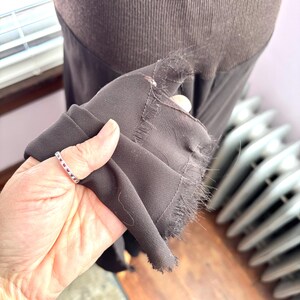 May include: A close-up of a dark brown garment, possibly a dress or skirt, with a frayed edge. The fabric appears to be a soft, flowing material. The garment is held up, revealing the texture and color.