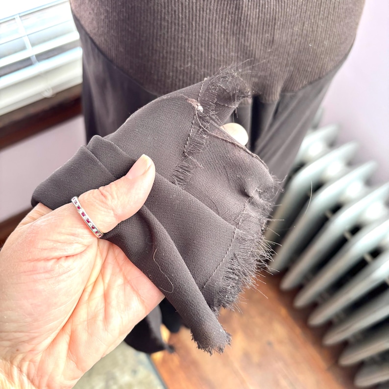 May include: A close-up of a dark brown garment, possibly a dress or skirt, with a frayed edge. The fabric appears to be a soft, flowing material. The garment is held up, revealing the texture and color.