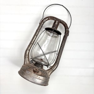 May include: Vintage metal lantern with a clear glass globe and a black top. The lantern has a handle for carrying and a weathered, rustic appearance. The lantern is made of metal and glass.