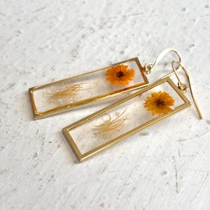 May include: Gold rectangle earrings with dried flowers and grass encased in clear resin.