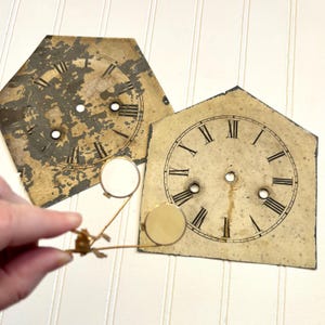 May include: Two antique clock faces with Roman numeral markings. The clock faces are made of metal and have a distressed, aged look. One clock face is hexagonal and the other is shaped like a house.