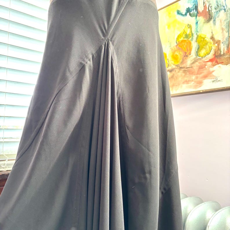 May include: A long, flowing black skirt with a pleated front panel. The skirt appears to be made of a smooth, lightweight fabric. The design features a high waist and a subtle A-line silhouette, suitable for various occasions.