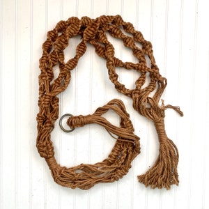 May include: A brown macrame plant hanger with a metal ring. The hanger has a tassel at the bottom.