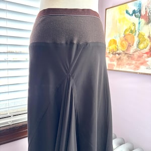 May include: A black skirt with a brown ribbed waistband. The skirt has a flowing, A-line silhouette. The waistband is a darker brown color, and the skirt is a solid black. The skirt is displayed on a mannequin.