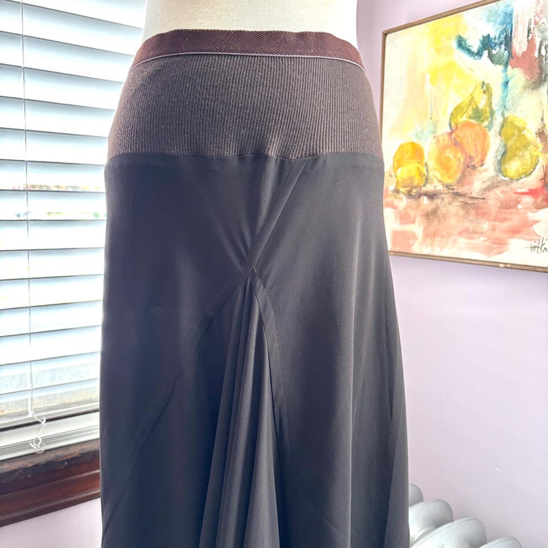 May include: A black skirt with a brown ribbed waistband. The skirt has a flowing, A-line silhouette. The waistband is a darker brown color, and the skirt is a solid black. The skirt is displayed on a mannequin.