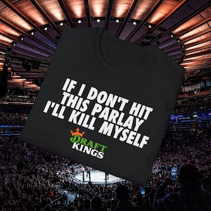 May include: Black t-shirt with the text "IF I DON'T HIT THIS PARLAY I'LL KILL MYSELF" in white. The Draft Kings logo is below the text in green and orange. The shirt is displayed in a crowded arena.
