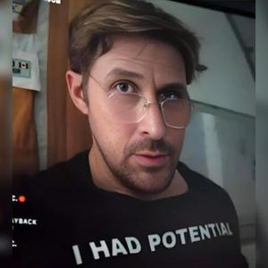 Könnte beinhalten: Eine Person mit einer Brille mit klarem Rahmen und getönten Gläsern und einem schwarzen T-Shirt. Das Shirt trägt den Text "I HAD POTENTIAL" in weißen Blockbuchstaben. Die Person hat hellbraunes Haar und einen Bart.