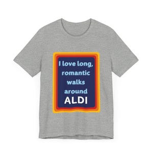 Puede incluir: Una camiseta gris con un rectángulo azul con el texto "Me encantan los largos paseos románticos alrededor de ALDI" en un borde de colores arcoíris.