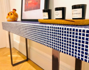 May include: A blue and white tiled console table with black metal legs. The table has a wooden top with three candles on it. The candles are labeled "Burning Rose", "Morning Rose", and "Bibliotheque".