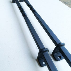 May include: Two black metal door handles with a twisted design. The handles are attached to square plates with a single screw hole.