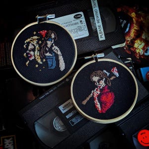 Può includere: Due cerchi da ricamo neri con disegni a punto croce colorati. Il primo cerchio presenta una donna con i capelli rossi e una camicia blu che tiene un coltello. Il secondo cerchio presenta una donna con i capelli castani e un vestito rosso che tiene un'ascia. Il testo "A Nightmare on Elm Street" è visibile su un nastro VHS sullo sfondo.