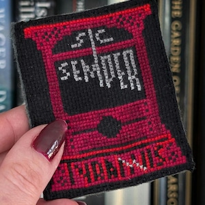 May include: A black and red embroidered patch with the words "SEMPER" and "HONORIS" in white thread. The patch has a rectangular shape with a decorative border and a central design.