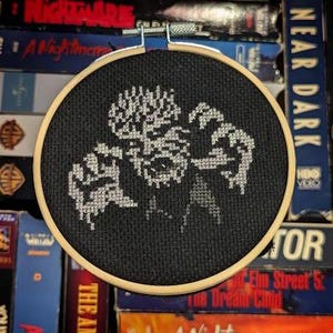 May include: A black cross-stitch embroidery hoop featuring a white pixelated design of a monster. The design is set against a black background. The wooden hoop is round and has a metal clasp.