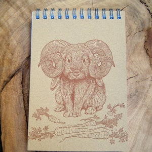 May include: A brown spiral bound notebook with a brown rabbit with ram horns and carrots printed on the cover.