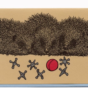 May include: Three brown hedgehogs with prickly fur are lying down on a tan background. A red ball and several black jacks are scattered in front of them.