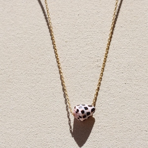 May include: A gold chain necklace with a pendant. The pendant has a pink base with black spots. The necklace is displayed against a neutral background. The chain is a delicate design.