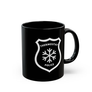 以下が含まれることがあります： 「THERMOSTAT POLICE」の文字と雪の結晶が描かれた白い警察バッジのデザインが特徴の黒いセラミックマグカップ。マグカップは湾曲したハンドルと光沢のある仕上げが施されています。