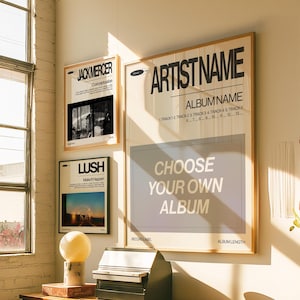 Può includere: Una collezione di poster incorniciati con copertine di album e testo, tra cui "JACK MERCER Conceptualize", "LUSH Make It Happen" e un poster personalizzabile che dice "CHOOSE YOUR OWN ALBUM". Un giradischi e una lampada sono su un mobile di legno.
