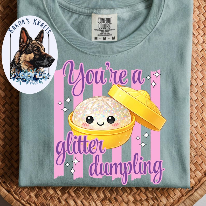 May include: A light blue t-shirt with a graphic of a glitter dumpling in a yellow container, with the text "You're a glitter dumpling" in purple. The shirt also features a logo with a German Shepherd dog.