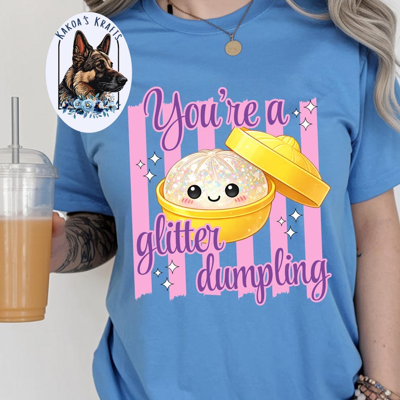 May include: A light blue t-shirt with a graphic of a glitter dumpling in a yellow bowl. The text "You're a glitter dumpling" is written in a cursive font. The shirt also has pink vertical stripes.