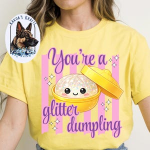May include: Yellow t-shirt with a graphic of a glitter dumpling in a yellow bowl with a lid. The text "You're a glitter dumpling" is in purple script with pink stripes.