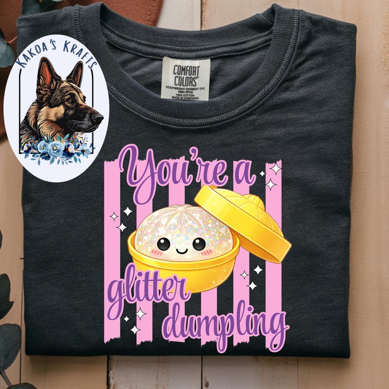 May include: Dark gray t-shirt with a graphic that says "You're a glitter dumpling." The graphic features a cute, glittery dumpling in a yellow bowl with a lid. The shirt also has a logo of a German Shepherd.