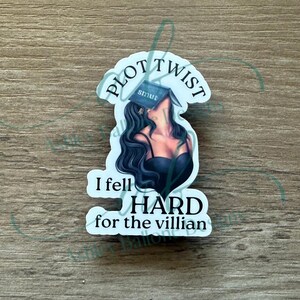 May include: A white sticker with black text that reads "Plot Twist I fell hard for the villian". A woman with long black hair is depicted with a book over her head that reads "smut".