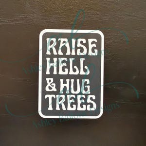 May include: Black and white sign with the text "Raise Hell & Hug Trees" in a retro font.
