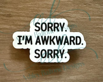 May include: A white sticker with the text "SORRY. I'M AWKWARD. SORRY." in black, with a rounded rectangular shape. The sticker is on a wooden surface.