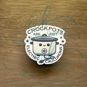 May include: White sticker with a cartoon slow cooker with a smiling face. The text reads "Crockpots are just electric cauldrons".