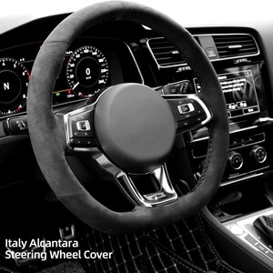 May include: A black steering wheel cover with a black suede-like material. The cover has a silver trim and stitching. The steering wheel has buttons on the left and right sides. The text "Italy Alcantara Steering Wheel Cover" is visible at the bottom of the image.