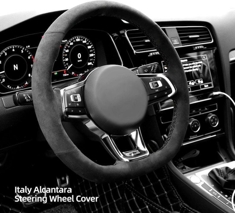 May include: A black steering wheel cover with a black suede-like material. The cover has a silver trim and stitching. The steering wheel has buttons on the left and right sides. The text "Italy Alcantara Steering Wheel Cover" is visible at the bottom of the image.