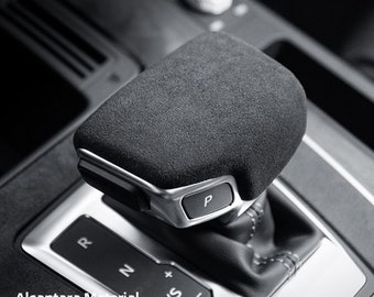 May include: Close-up of a black Alcantara gear shift knob cover for Audi. The cover is made of soft, suede-like material and features a silver trim around the edges. The gear shift knob has a silver button labeled "P" for park.