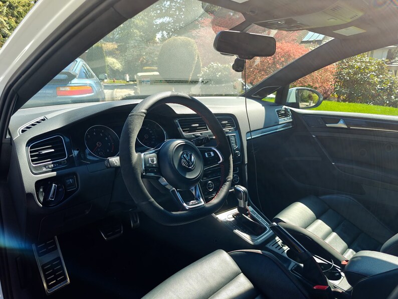 May include: The interior of a black car with a black leather steering wheel, black leather seats, and a black dashboard. The car has a sunroof and a rearview mirror. The car is parked in a driveway.