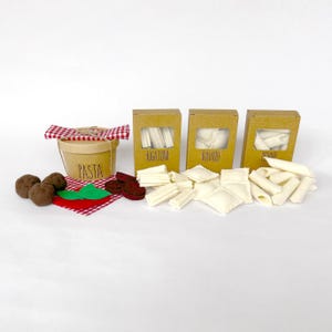 May include: A collection of felt pasta and accessories. Includes a wooden bucket labeled "PASTA", boxes of rigatoni, ravioli, and penne, felt meatballs, and a red and white checkered napkin.