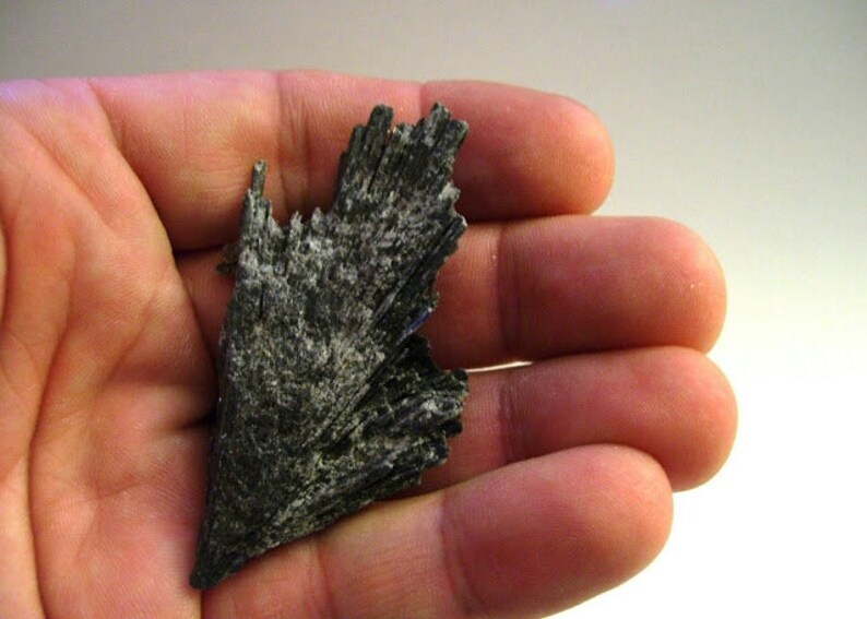 May include: A dark gray, naturally formed, mineral specimen with a pointed tip and a layered, fan-like structure.