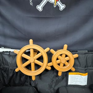 May include: Two wooden ship steering wheels in different sizes, with a light brown finish. The wheels are set against a black background, with a skull and crossbones logo and the text "WONDERFOLD" visible above.