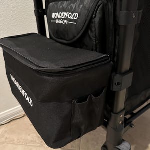 May include: Black Wonderfold Wagon with a side storage bag. The bag has the Wonderfold logo in white. The wagon has a black frame and wheels. The storage bag has two small pockets on the side.
