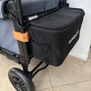 May include: A black and gray utility wagon with a black cooler bag attached. The cooler bag has the word "WONDERFOLD" printed on it. The wagon has a black frame, gray fabric, and black wheels. An orange-colored wooden piece is attached to the frame.