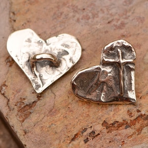 May include: Two silver heart-shaped charms, one with a cross design and the other with a loop for attaching to a necklace or bracelet.