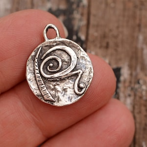 May include: Silver pendant with a hammered texture and a spiral design. The pendant is round and has a loop at the top for attaching a chain.