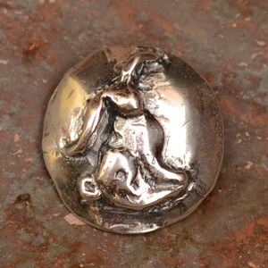 May include: A silver charm featuring a detailed rabbit sculpture. The charm is round and has a textured surface.
