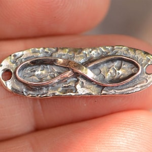 May include: Silver infinity charm with a textured finish and two holes for attaching to jewelry.