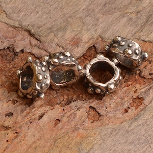 May include: Four silver metal bead spacers with a textured surface. Each spacer has a round hole in the center.