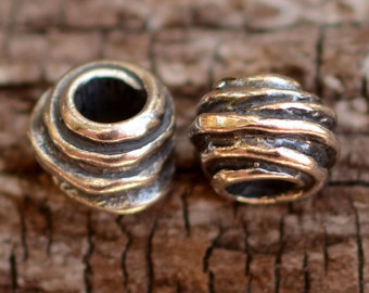 May include: Two silver metal beads with a textured, wavy design. The beads are round and have a hole in the center.