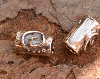 May include: Two silver metal beads with textured surfaces. One bead has a swirl design and the other has a smooth surface.