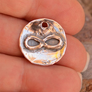 May include: A silver charm with an infinity symbol design. The charm has a textured surface and a hole at the top for attaching to a necklace or bracelet.