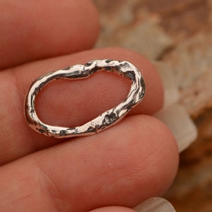 May include: A silver oval ring with a textured, organic design. The ring is made of sterling silver and has a rustic, handmade look.