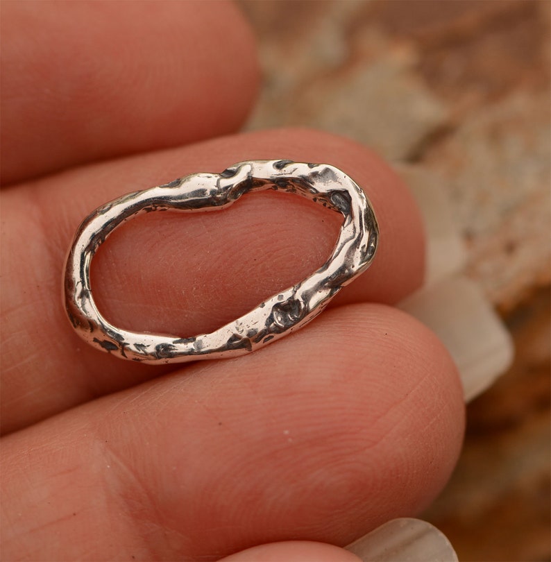 May include: A silver oval ring with a textured, organic design. The ring is made of sterling silver and has a rustic, handmade look.