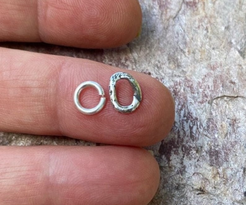 May include: Two silver jump rings, one smooth and one textured, are shown on a finger.